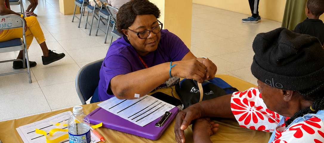 Hope for Humanity volunteer in purple shirt taking blood pressure at indoor community clinic