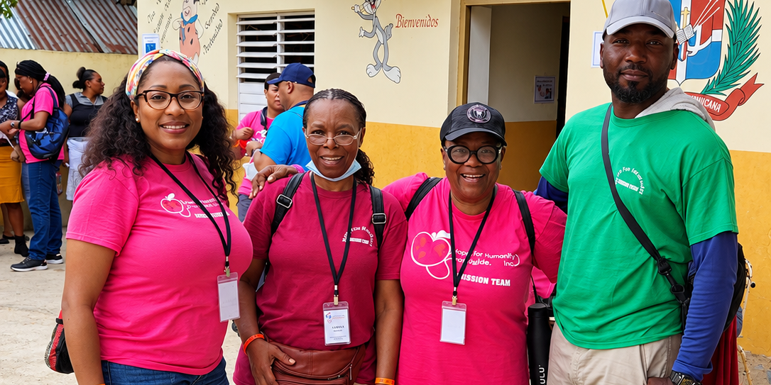 Hope for Humanity mission team in pink and green shirts posing together outside a community building