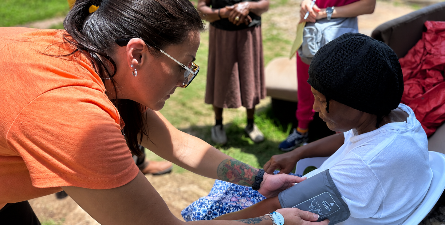 Hope for Humanity volunteer in orange shirt taking blood pressure outdoors