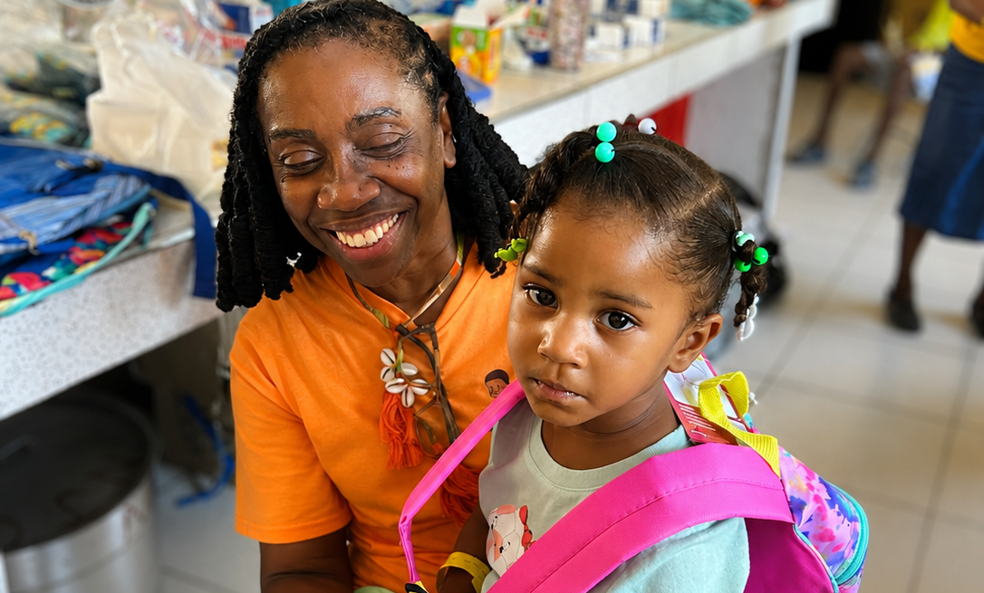Hope for Humanity volunteer joyfully helping toddler try on a pink backpack