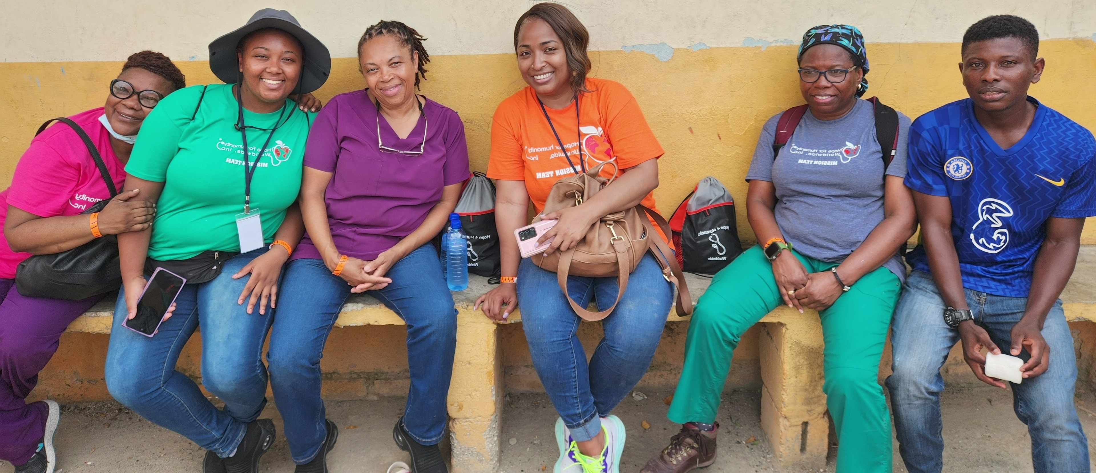 Six Hope for Humanity mission team members sitting together relaxing against a yellow wall